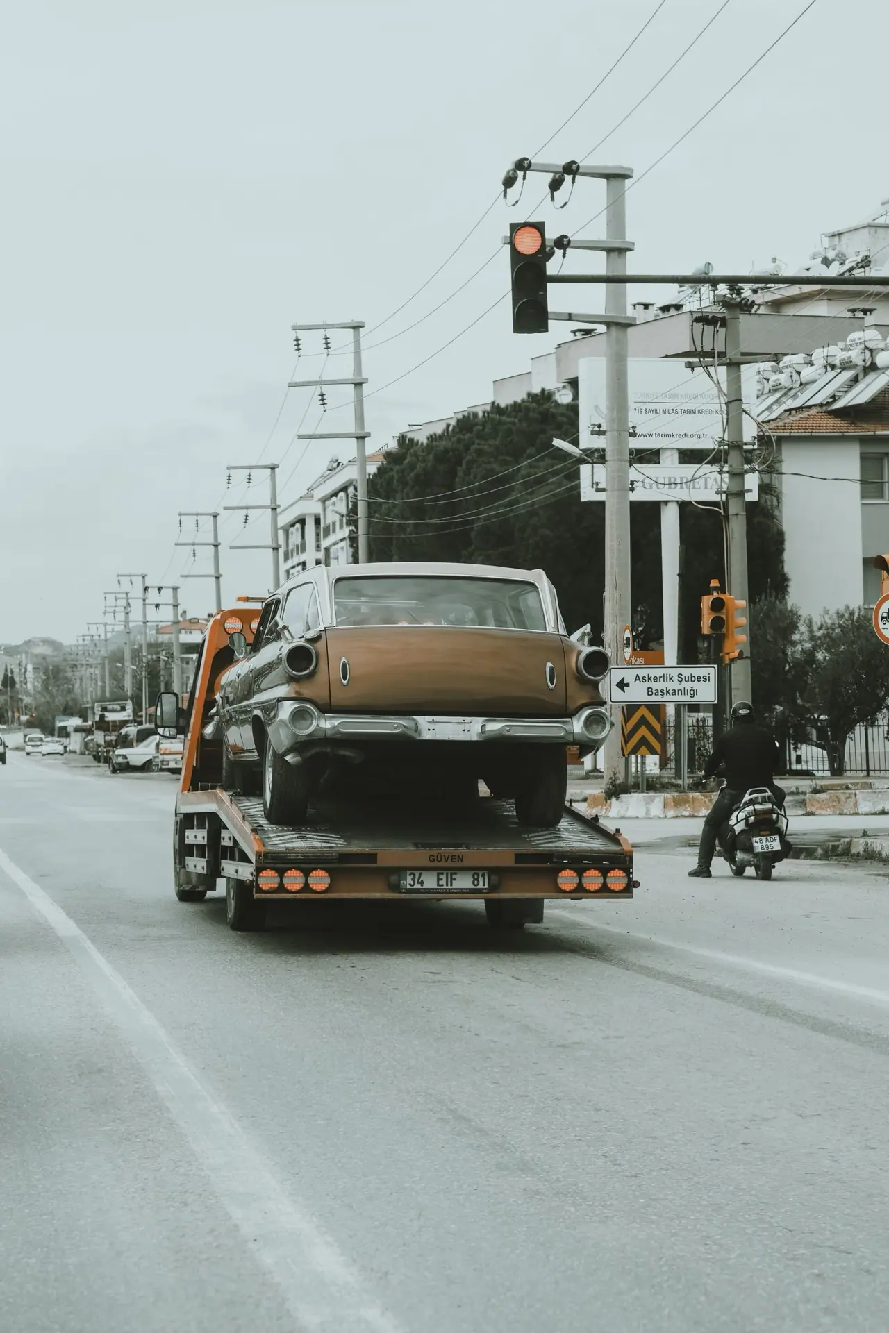 A tow truck carrying a vintage car down a city street