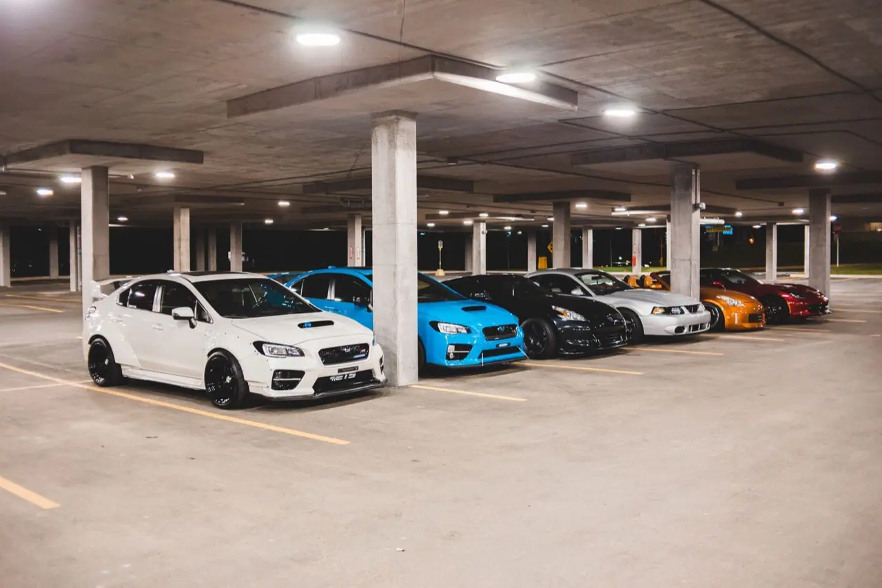 Sports cars parked indoors between concrete columns under bright lights
