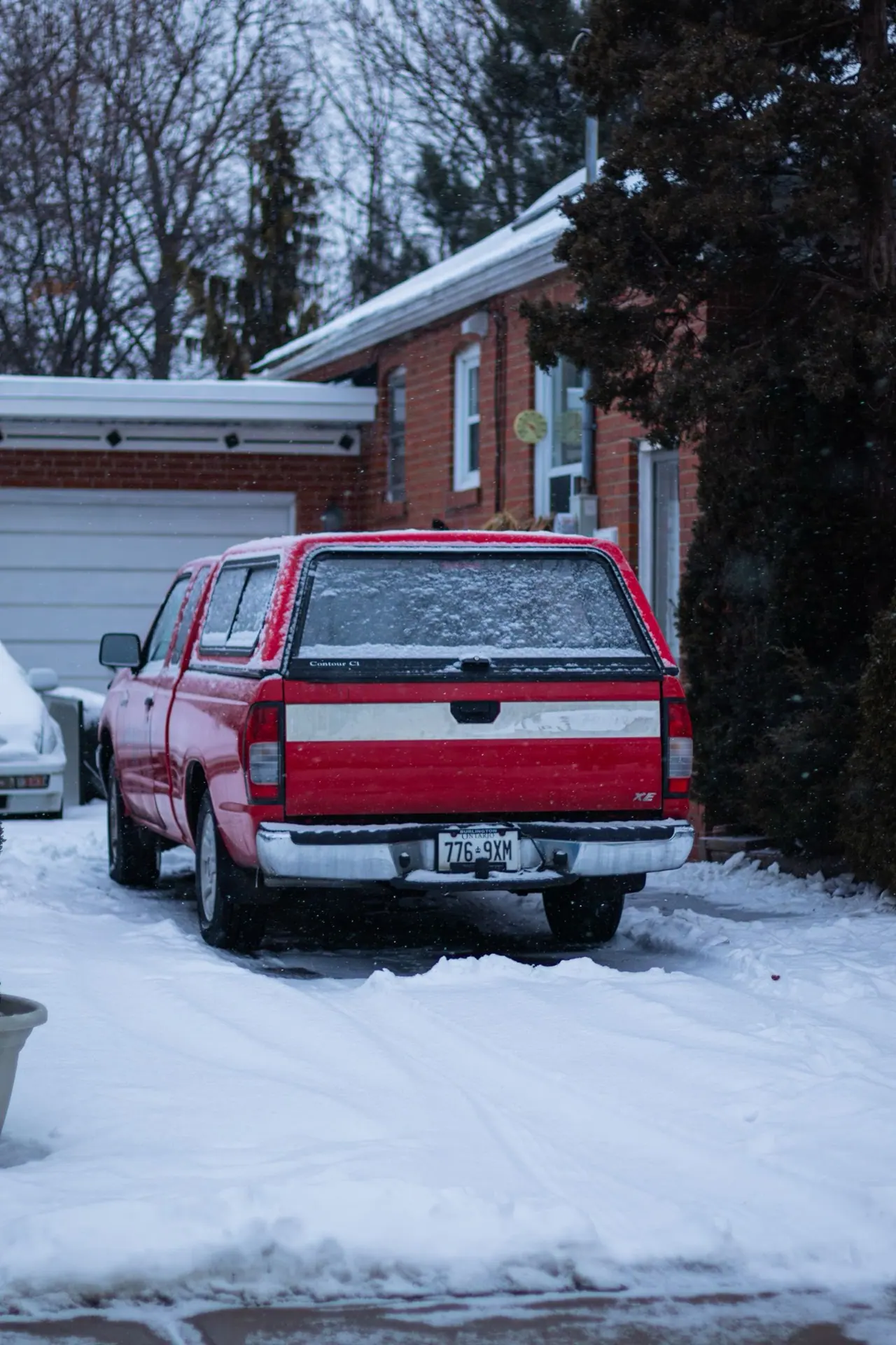 A red pickup truck parked in a snowy suburban driveway in Toronto