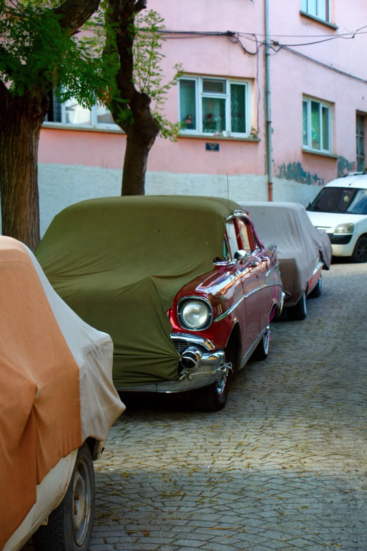A vintage car partly covered with fabric on a street