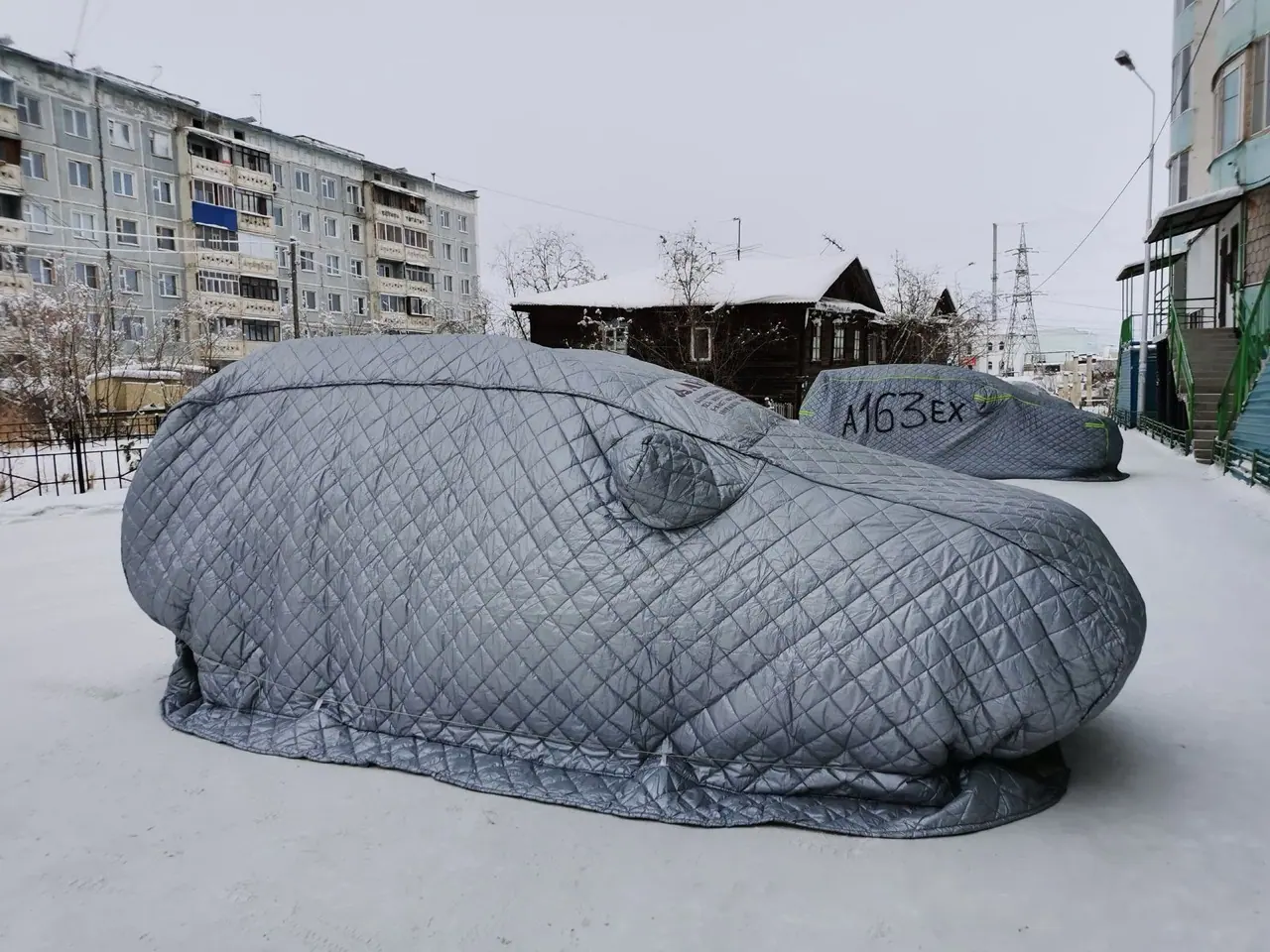 A car under a quilted winter cover standing in fresh snow